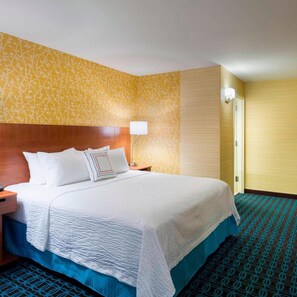 A hotel room with a large bed, a wooden headboard, a nightstand, a lamp, and a patterned carpet. - Fairfield Inn Suites By Marriott Paramus (Paramus)