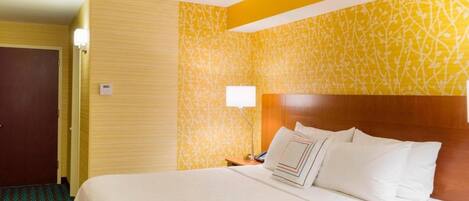 Habitación de hotel con una cama grande, cabecera de madera, mesita de noche con lámpara y alfombra estampada.
