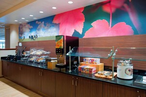 Un mostrador de buffet con diversos alimentos, una máquina de café y un amplio mural floral en la pared.