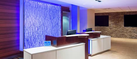 A reception area with a modern design, featuring a reception desk, a decorative wall with blue lighting, a stone wall, and a mounted television.