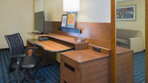 A hotel room with a wooden desk, a black office chair, a lamp, a framed picture, and a couch. - Fairfield Inn Suites By Marriott Paramus (Paramus)