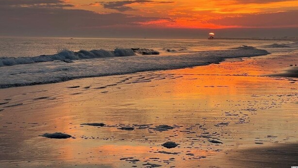 Ein Strand bei Sonnenuntergang mit einem Steg, der sich ins Wasser erstreckt.