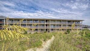 Ein mehrstöckiges Hotel mit Balkonen, einem Sandweg und dichter umliegender Vegetation.