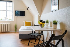 A modern bedroom with a bed, a bedside table with a fruit bowl, a chair, and a TV mounted on the wall. - Alte Feuerwache (Berlin)