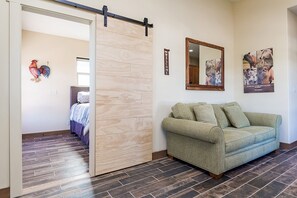 A room with a sliding door, a green sofa, a wooden floor, a bed with a blue and white bedspread, and a wall with a 'WELCOME' sign and a mirror.