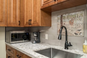 A kitchen with wooden cabinets, a stainless steel sink, a microwave, and a coffee maker.