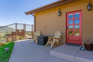 A patio with two Adirondack chairs, a small table, and a red door.