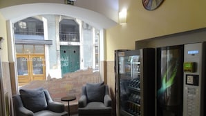 Une pièce comprenant deux fauteuils, une petite table, un distributeur automatique et une vue sur le paysage urbain, visible à travers une grande fenêtre.