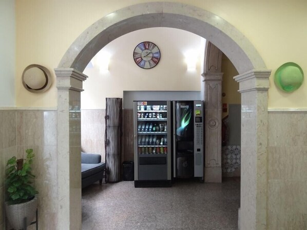 Un hall d’entrée avec un distributeur automatique, une horloge et un espace détente.
