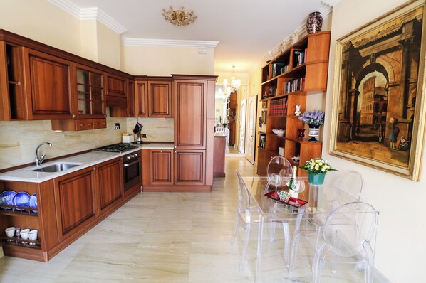 A spacious kitchen with wooden cabinets, a marble countertop, and a dining area with clear glass chairs and a table.