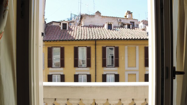 Un edificio amarillo con contraventanas marrones y techo de tejas.
