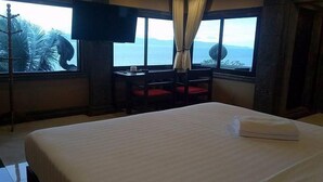 A hotel room with a bed, a desk, a chair, a TV, and a view of the sea. - Blue Hill Beach Resort (Ko Pha-ngan)