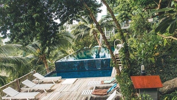 An infinity pool surrounded by lush greenery and wooden deck chairs. - Blue Hill Beach Resort (Ko Pha-ngan)