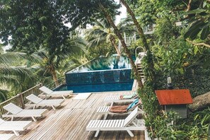 An infinity pool surrounded by lush greenery and wooden deck chairs. - Blue Hill Beach Resort (Ko Pha-ngan)