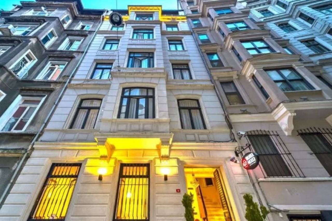A multi-story building with a classic architectural style, featuring symmetrical windows and a central entrance with a yellow-lit facade.