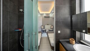 A modern bathroom with dark tiles, a glass shower enclosure, a sink, and a mirror. - Hotel Next2 (Istanbul)