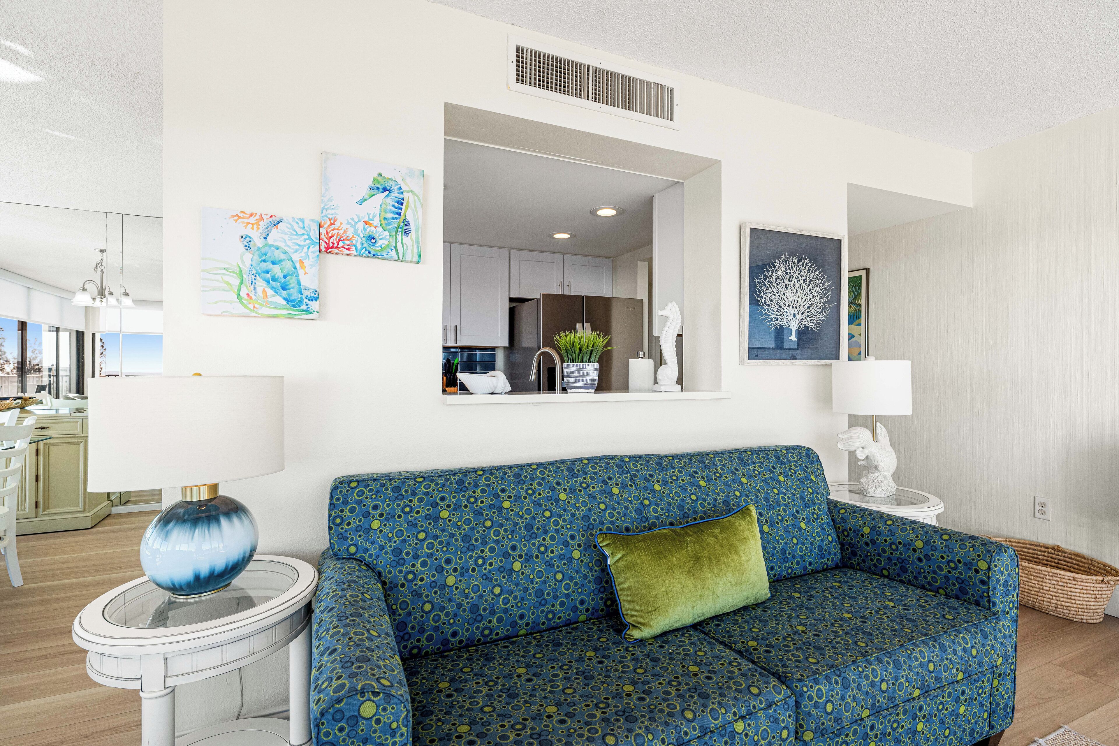 A modern living room with a blue patterned sofa, a round side table, and a kitchen visible through an archway.
