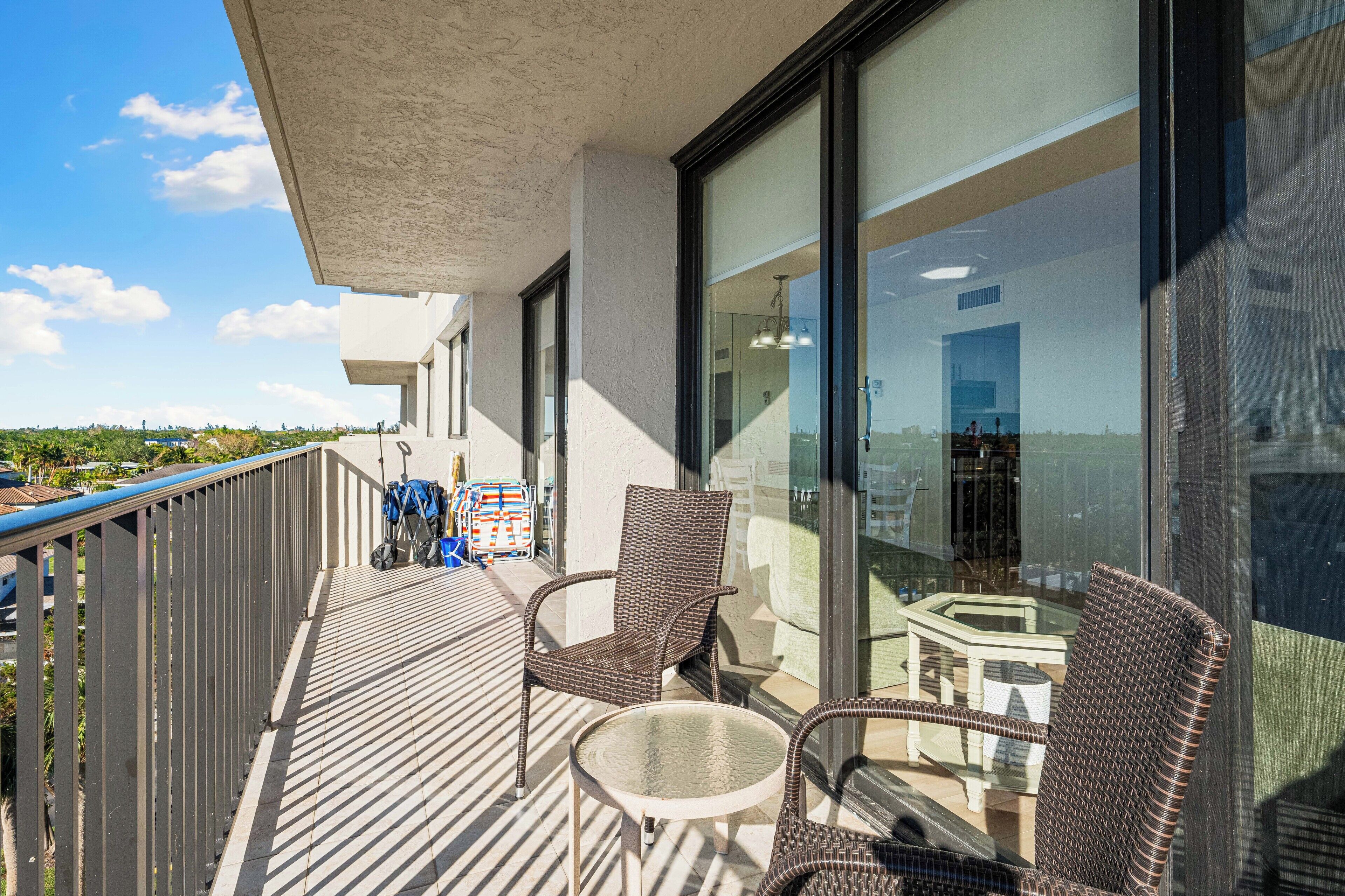 A balcony with wicker chairs and a small table, overlooking a cityscape.