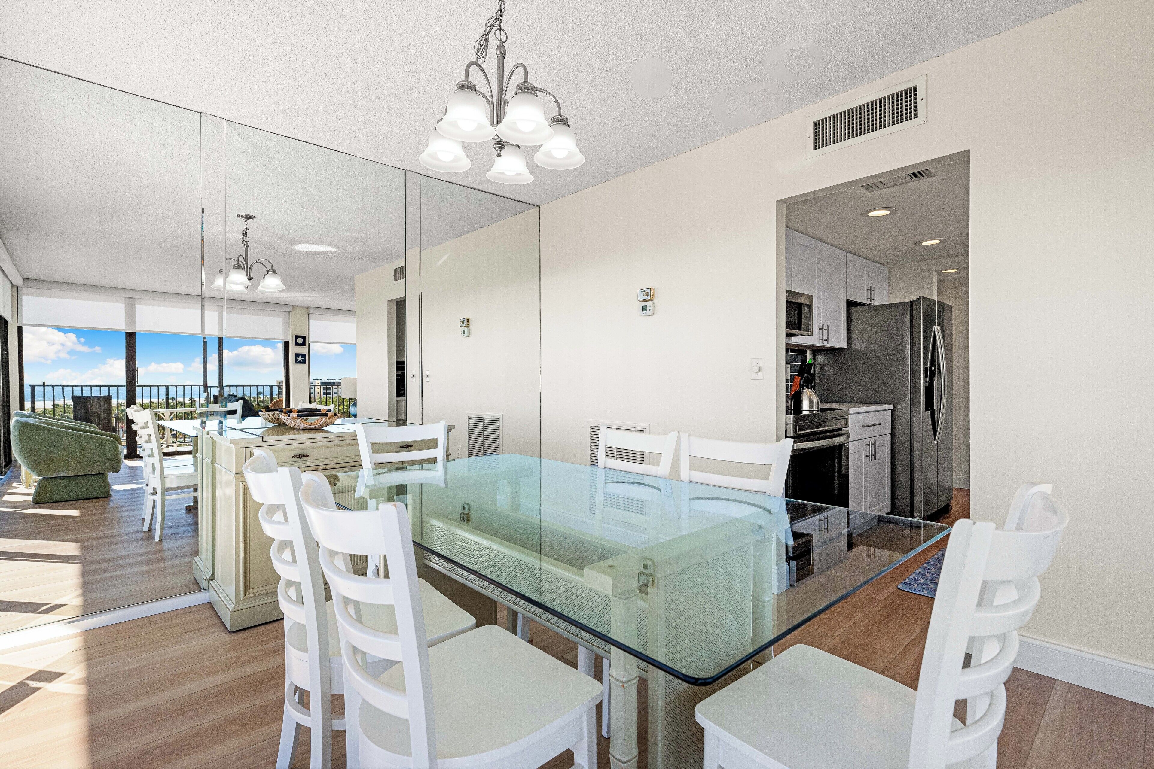 A modern kitchen with a glass dining table, white chairs, and stainless steel appliances.