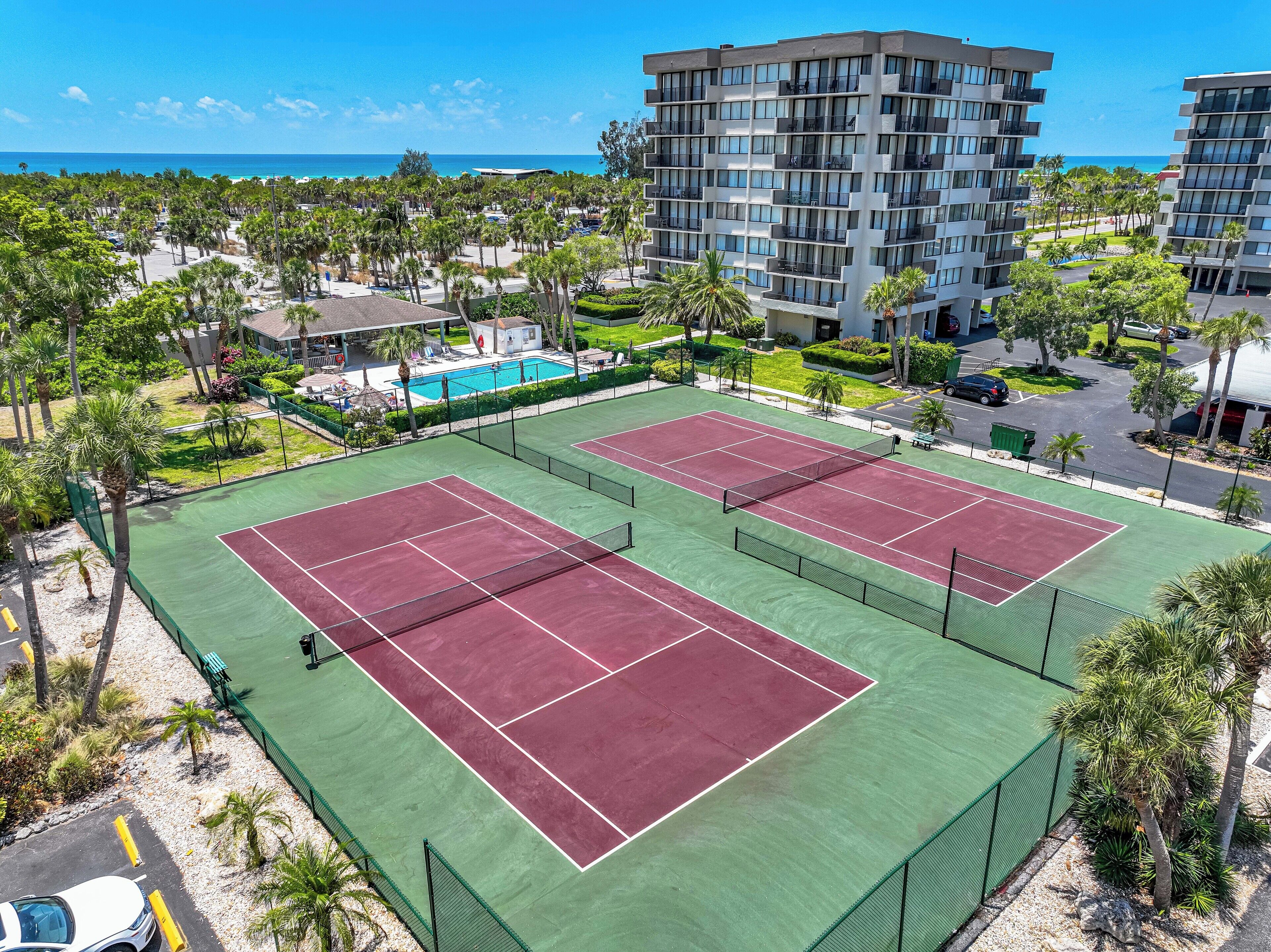 Un campo da tennis con piscina, circondato da palme e un edificio con balconi.