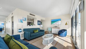 A modern living room with a blue sofa, a coffee table, and a blue armchair. There is a television mounted on the wall and a window providing natural light. - Stunning 2 Bedroom/ 2 Bath with Best Siesta Key Beach Views! (Siesta Key)
