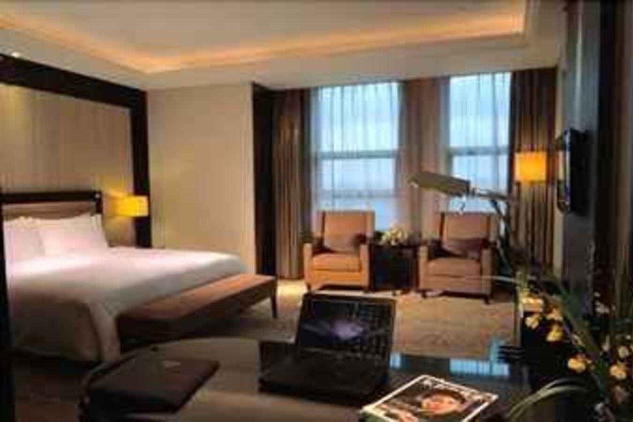 A hotel room with a bed, a desk, a chair, a lamp, and a TV.