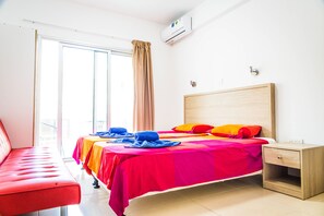 Une chambre d’hôtel lumineuse, dotée d’un grand lit, d’une table de chevet en bois et d’un banc rouge.