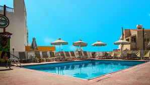 A swimming pool with lounge chairs and umbrellas, surrounded by buildings with visible signage. - Efi Hotel Apartments (Ayia Napa)