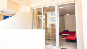 A room with a glass door leading to a balcony, a bed with a red cover, and a small table with a chair. - Efi Hotel Apartments (Ayia Napa)