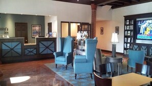 A lobby with a reception desk, seating area, and a television screen displaying a sports event. - The Flagler Inn (St. Augustine)