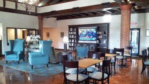 A lobby with a coffee bar, seating area, and a TV screen displaying a sports event. - The Flagler Inn (St. Augustine)