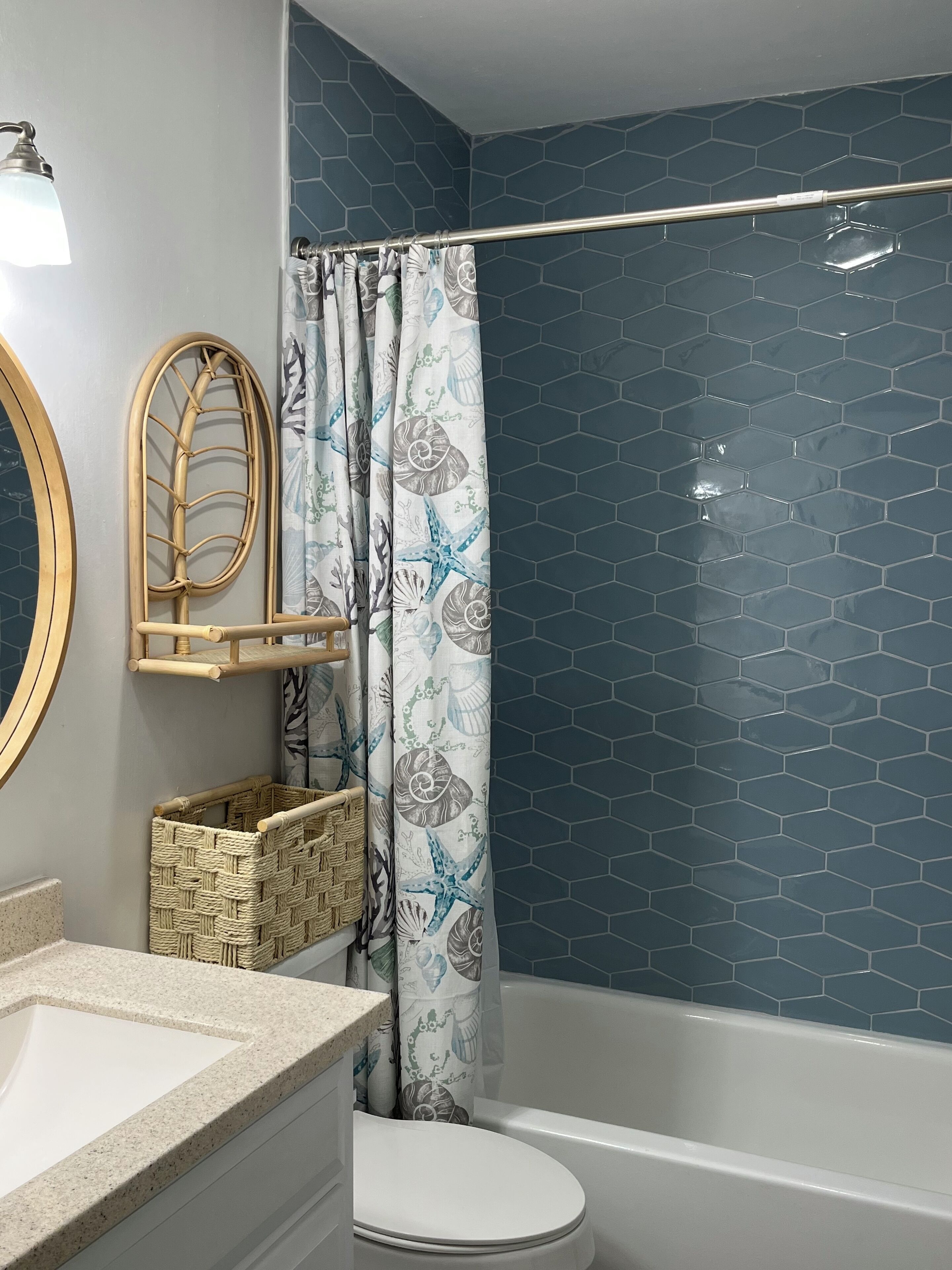 A bathroom with a white toilet, a white sink, a mirror, a shower curtain with a floral pattern, and a blue hexagonal tile wall.