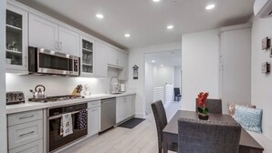 Une cuisine moderne avec des meubles blancs, un four à micro-ondes encastré et un coin repas comprenant une table et des chaises.
