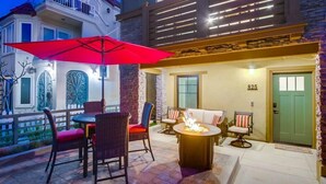 Un espace patio aménagé avec des meubles en osier, un parasol rouge et un foyer.