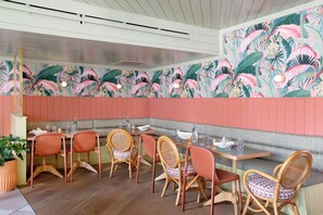 A restaurant with wooden chairs and tables, a bench along the wall, and a tropical mural on the wall. - The Ryder Hotel (Charleston)