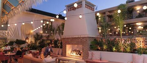 An outdoor seating area with wicker furniture, a fire pit, and string lights.