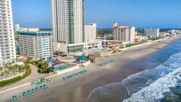 A coastal hotel with high-rise buildings, a beach, and a pool area.