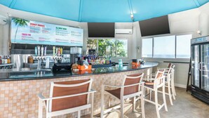 A bar area with a menu board, bar stools, and a refrigerator.