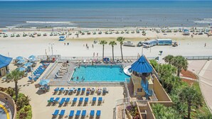 A resort with a swimming pool, beach umbrellas, and lounge chairs.