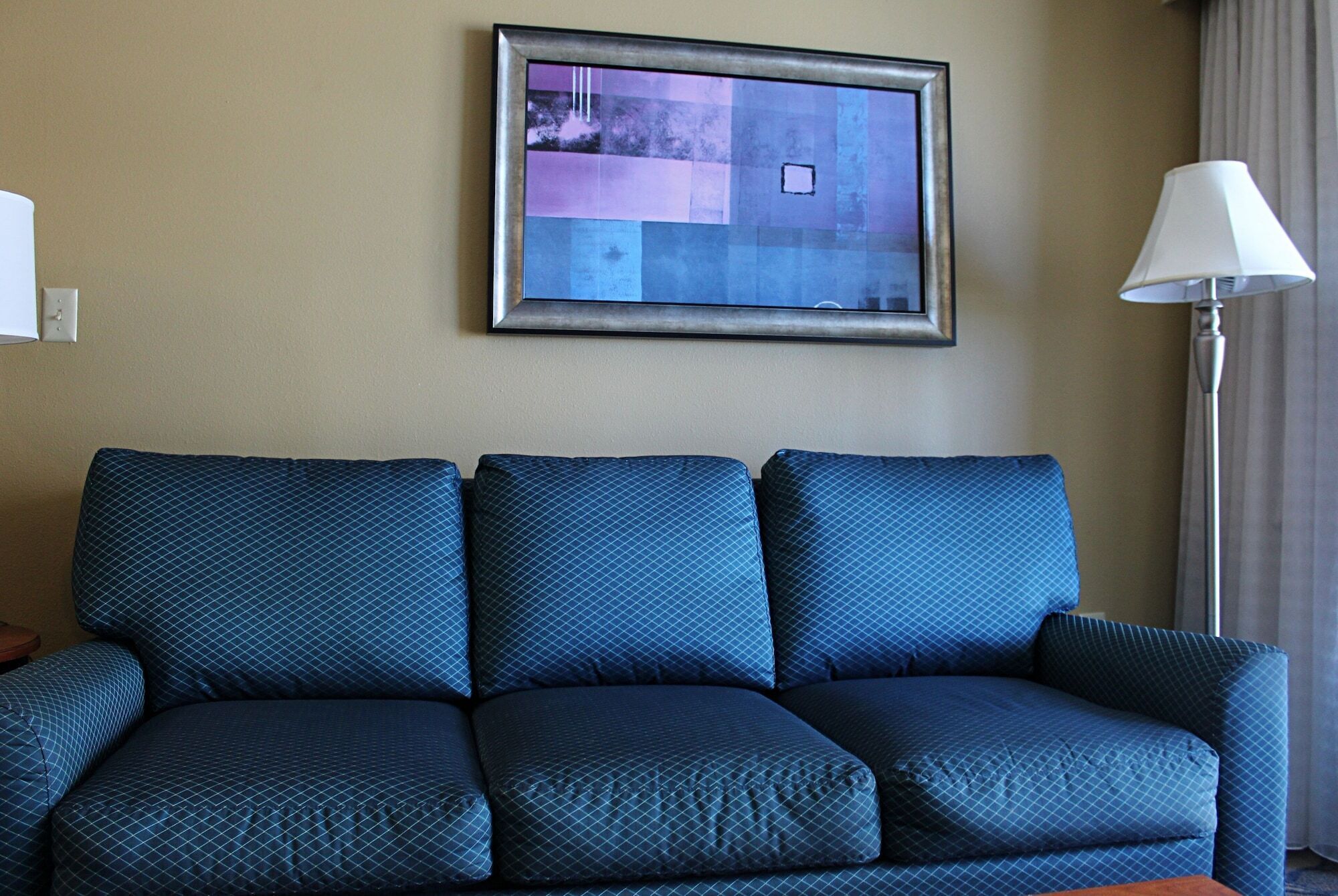 Ein Hotelzimmer mit einem dunkelblauen Sofa, einem gerahmten Bild an der Wand und einer Lampe auf der rechten Seite.