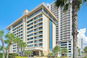 A multi-story hotel with a modern design, featuring balconies, a central atrium, and a landscaped outdoor area with palm trees. - Hilton Vacation Club Daytona Beach Regency (Daytona Beach)