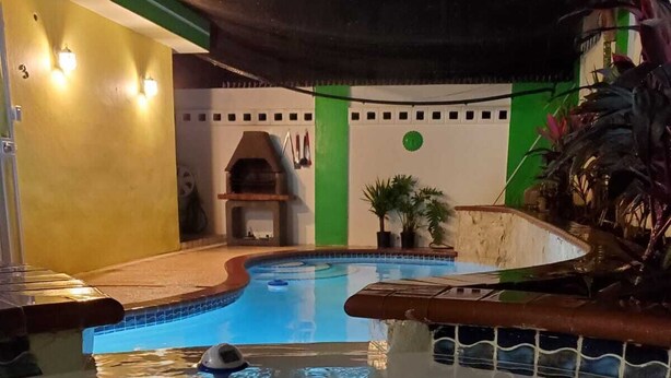 A swimming pool with a tiled edge, a barbecue area, and a green wall with a circular emblem. - La Casita Verde in Cupey - Villa with Pool-Hot Tub and POWER GENERATOR (San Juan)