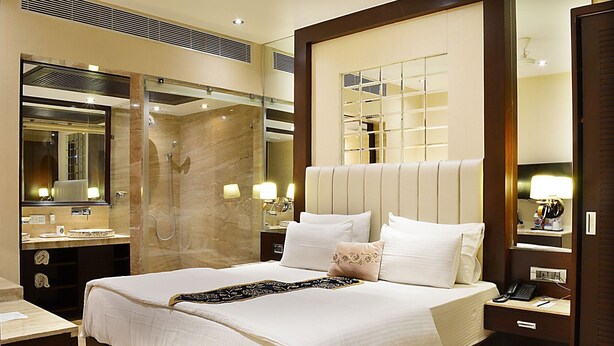 A hotel room with a large bed, a bathroom with a shower, and a minibar. - Hotel Emperor Palms (New Delhi)