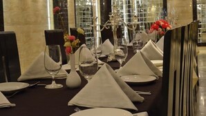 A dining table set with white napkins, plates, and glassware, with a vase of flowers and a decorative centerpiece. - Hotel Emperor Palms (New Delhi)