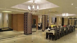 A spacious hotel lobby with a high ceiling, chandeliers, and a long dining area with tables and chairs. - Hotel Emperor Palms (New Delhi)