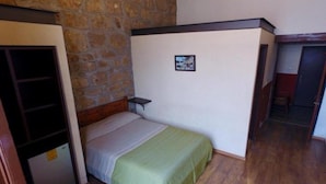 Una habitación pequeña y acogedora con una cama individual, un armario de madera y una pared de piedra.