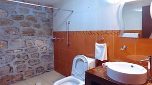 Un baño con pared de piedra, inodoro blanco, lavamanos y espejo.
