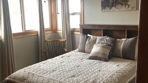 Ein Schlafzimmer mit einem großen Bett, einem Holzkopfende, einem Deckenventilator und einem Fenster mit Vorhängen.