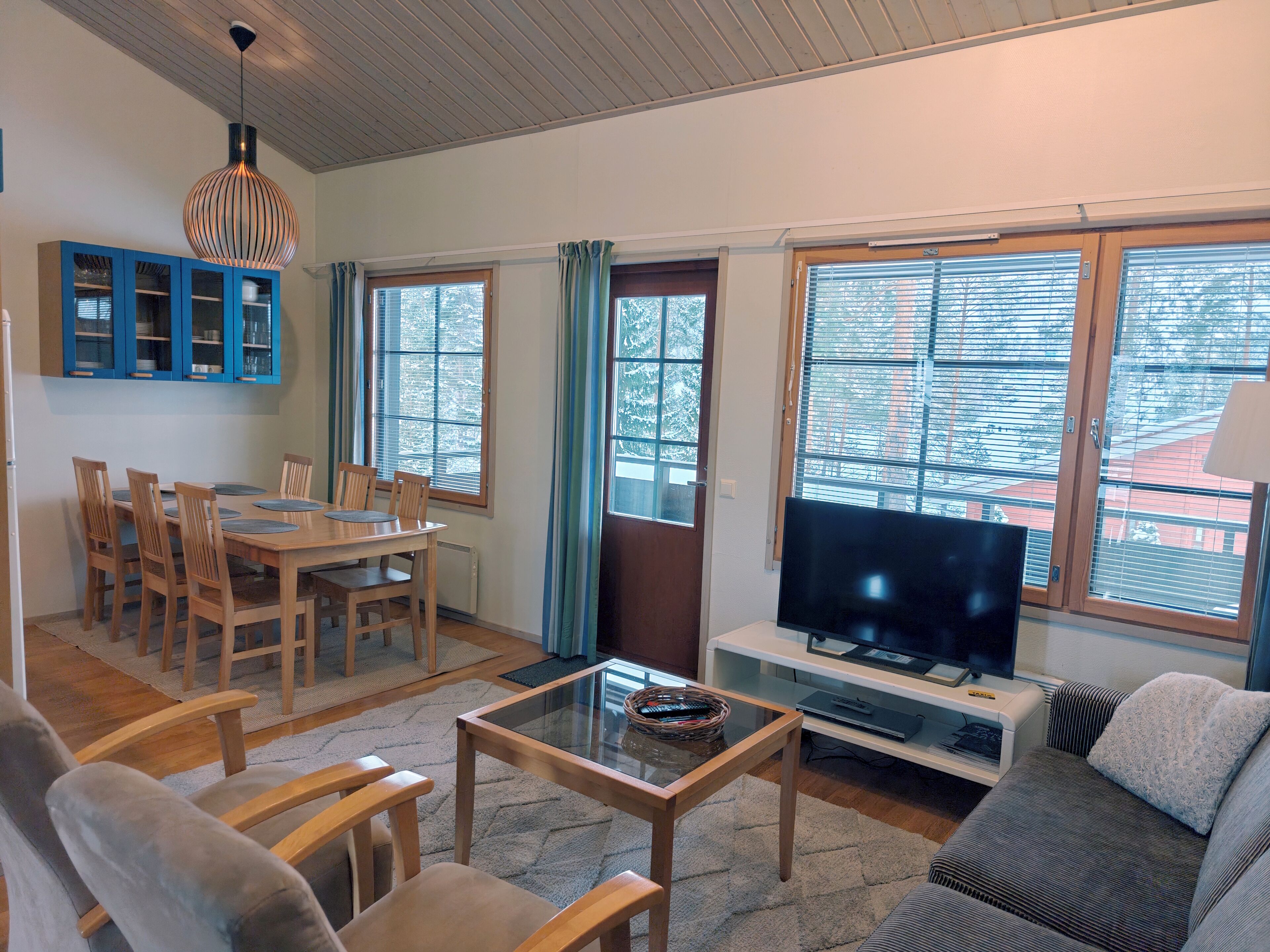 Una sala de estar con comedor, televisor y ventanas grandes.