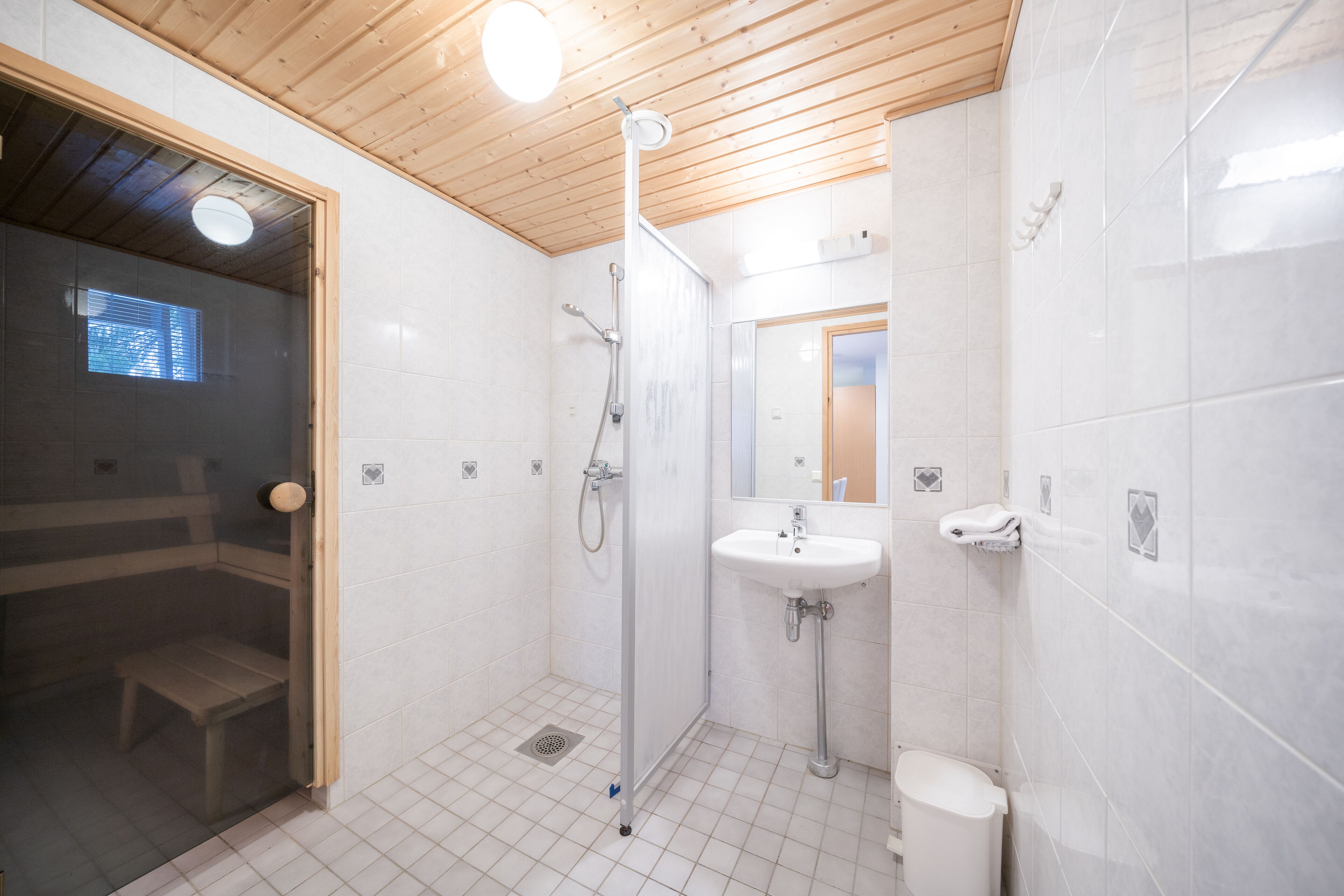 A modern bathroom with a wooden ceiling, a glass-enclosed shower, a white sink, and a toilet.